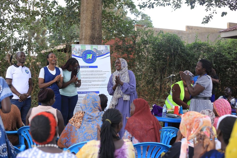 Team members addressing women seated under the trees at the community outreach